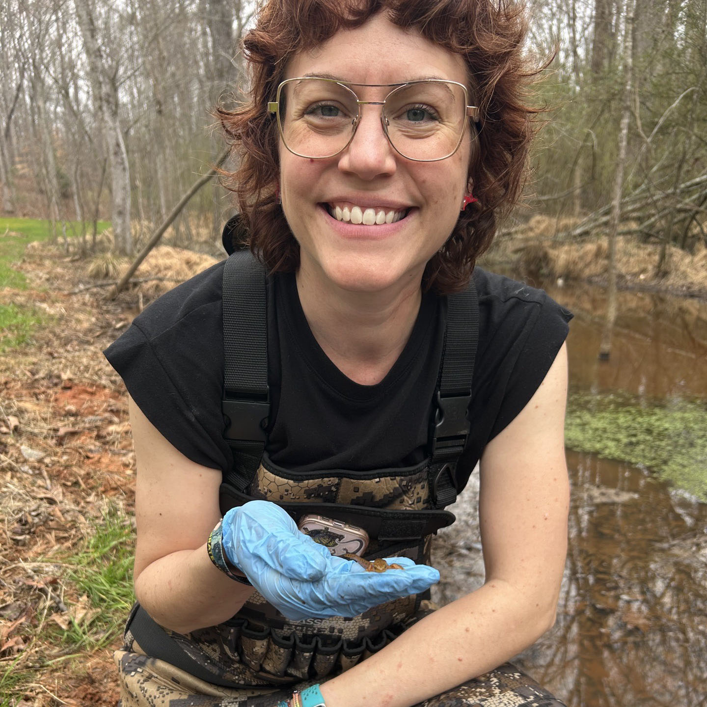 Leslie Day smiling, holding an eastern newt in front of a wetland.