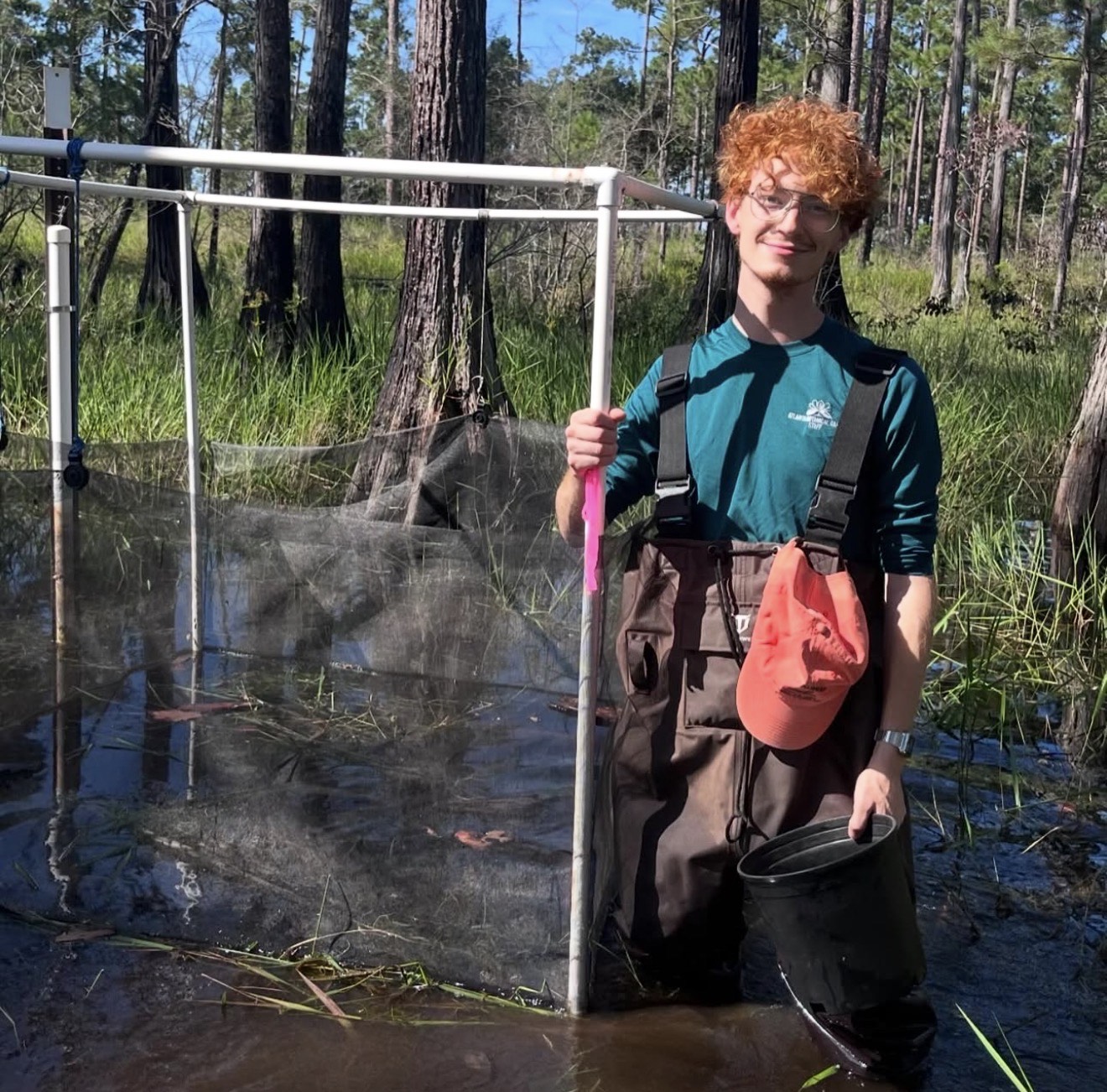 Sam Dill holding an enclosue in the shallows of a grassy wetland.