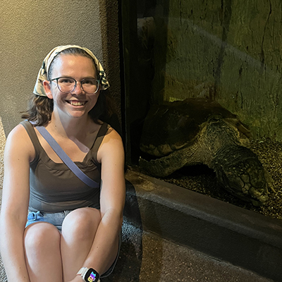 Hailey Wunder smiling, seated next to a turtle in an aquarium.